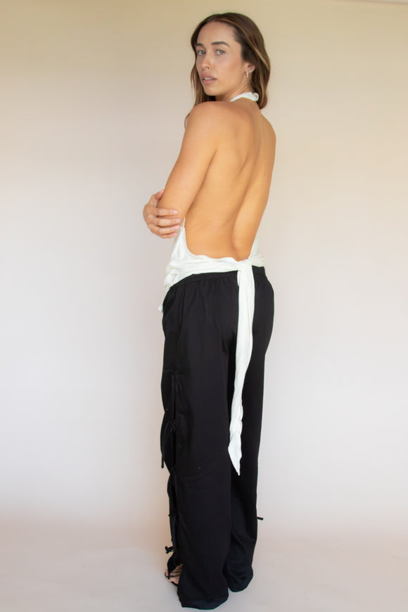 Woman wearing a black tie pants and a low back white halter top with a plain background