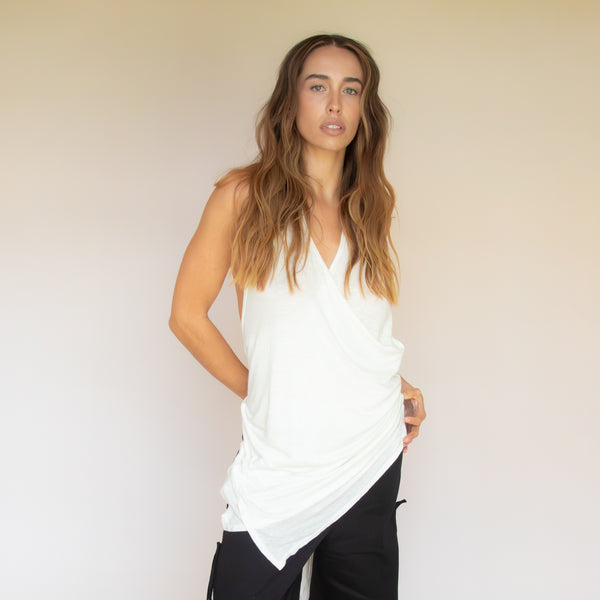 Woman wearing a white sleeveless wrap top and black pants against a plain background